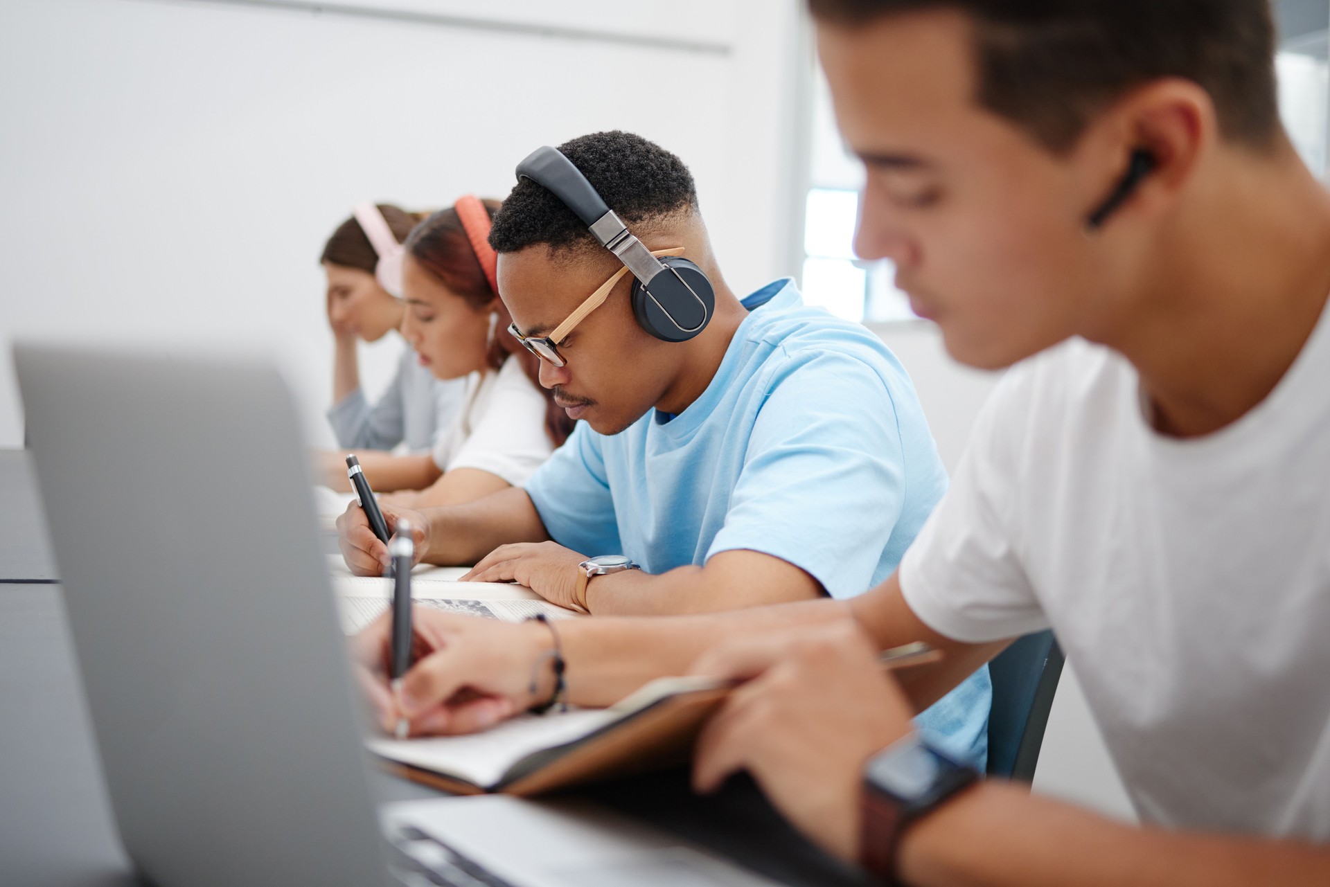 Student at university study, writing and research for a exam or project with headphones for podcast or music. College, school or education black man learning, scholarship and studying in campus hall